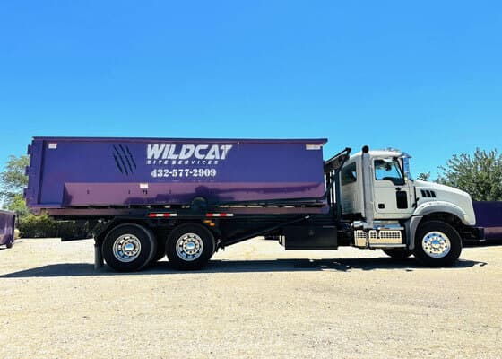 Wildcat Site Services truck carrying a purple roll-off dumpster